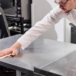 Chef wiping a stainless steel prep table with a disposable wiping cloth in a commercial kitchen