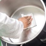 Worker wiping the inside of a stainless steel mixing vessel with a low-lint nonwoven wipe