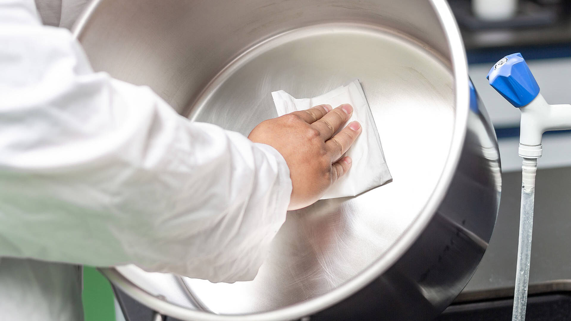 Worker wiping the inside of a stainless steel mixing vessel with a low-lint nonwoven wipe