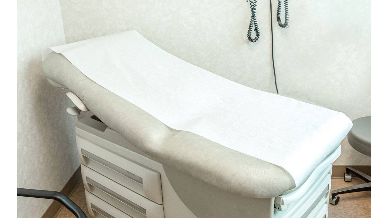 Examination table covered with disposable exam table paper in a clinic exam room