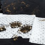 White oil-only absorbent pads laid over spilled oil, soaking it up during an oil spill cleanup