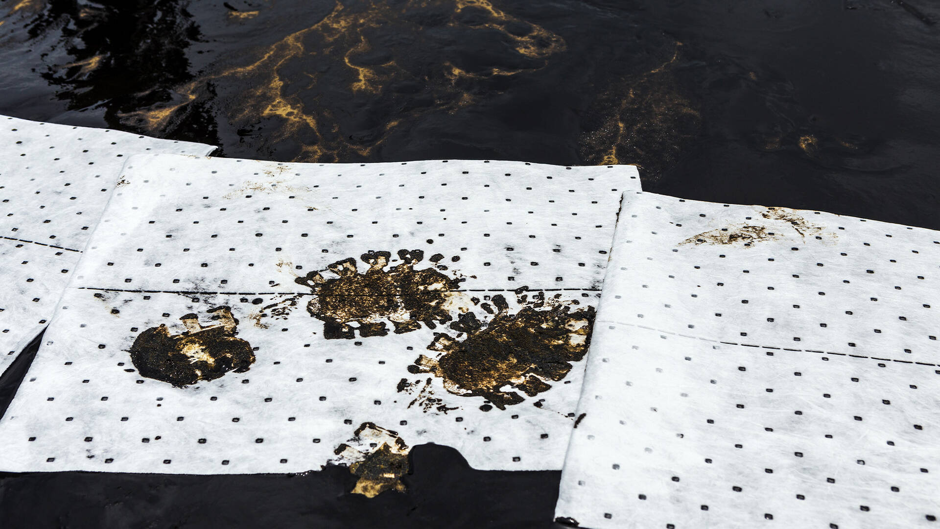 White oil-only absorbent pads laid over spilled oil, soaking it up during an oil spill cleanup