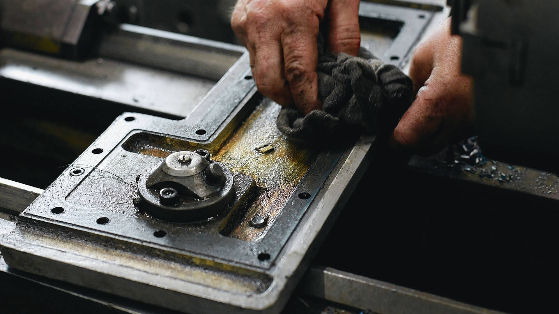 Hands wiping an oily machine tool table with a grey cloth shop towel