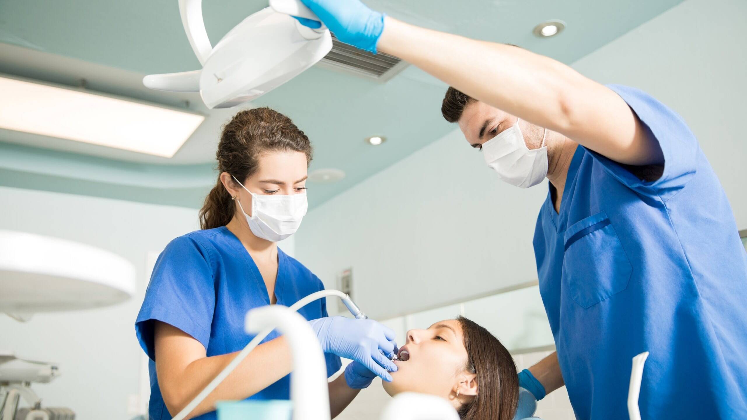 Dental team treating a patient in a dental chair, wearing masks and gloves