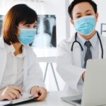 Kakitangan perubatan memakai pelitup muka prosedur sambil menyemak rekod pesakit pada komputer riba