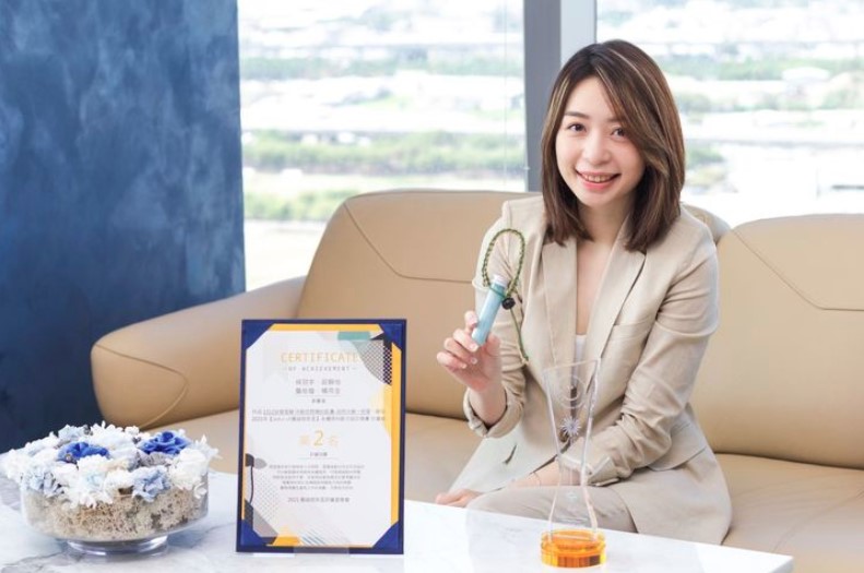 A presenter demonstrates a material sample beside a certificate during an interview