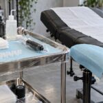 Tattoo station set up with a blue dental bib on a wrapped tray cart, a covered tattoo bed and a wrapped armrest